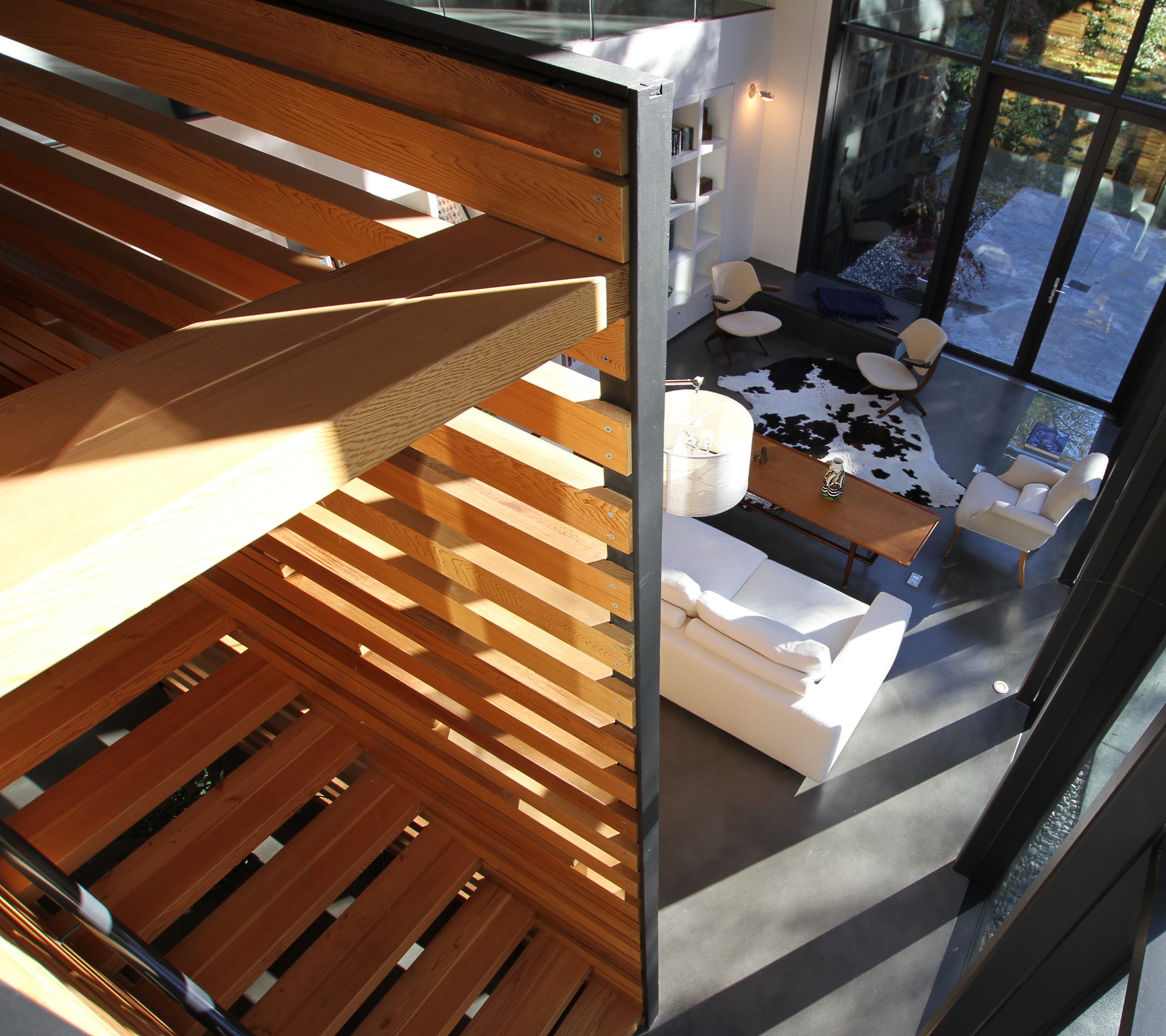 Living room with white furniture, large windows, and wooden staircase viewed from above—showcasing the quality design you’d expect from a reputable company specializing in custom homes.