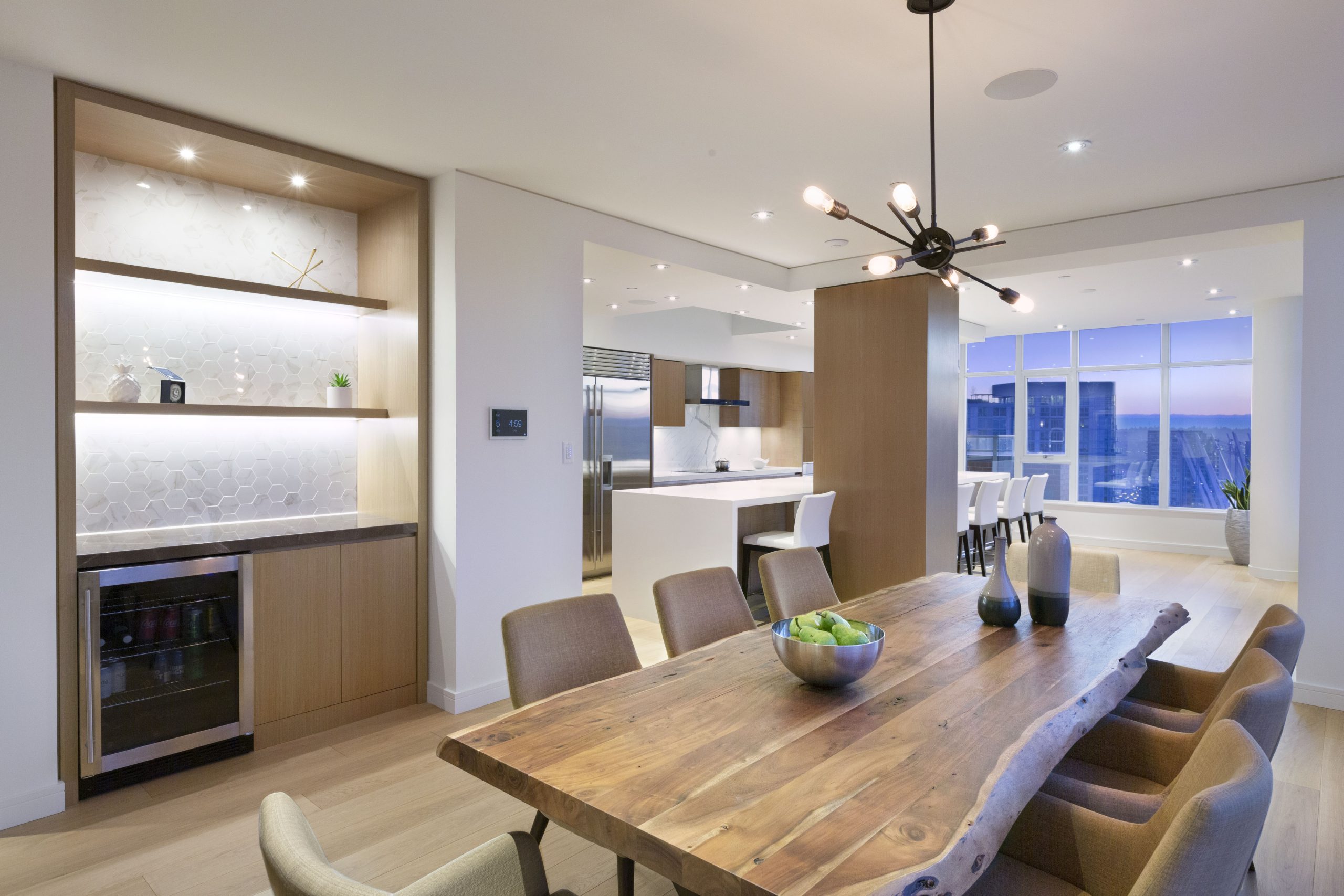 Open kitchen and dining area with a wooden table, stylish chairs, and large windows with city views—showcasing innovative architecture ideal for custom homes in Vancouver
