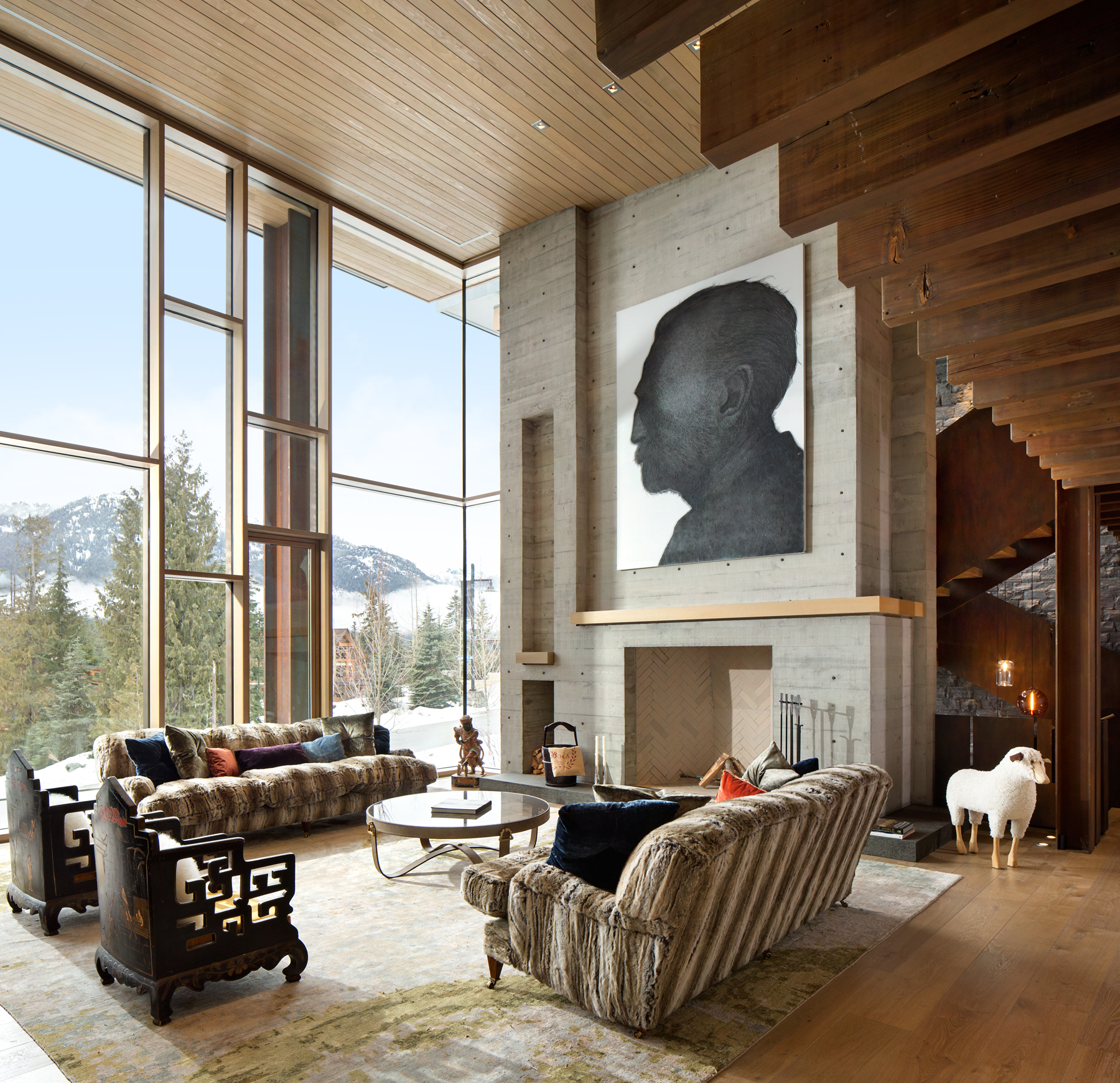 Spacious living room with large windows, mountain view, two sofas, art above fireplace, and a decorative white sheep. Designed by a leading Vancouver general contractor company.
