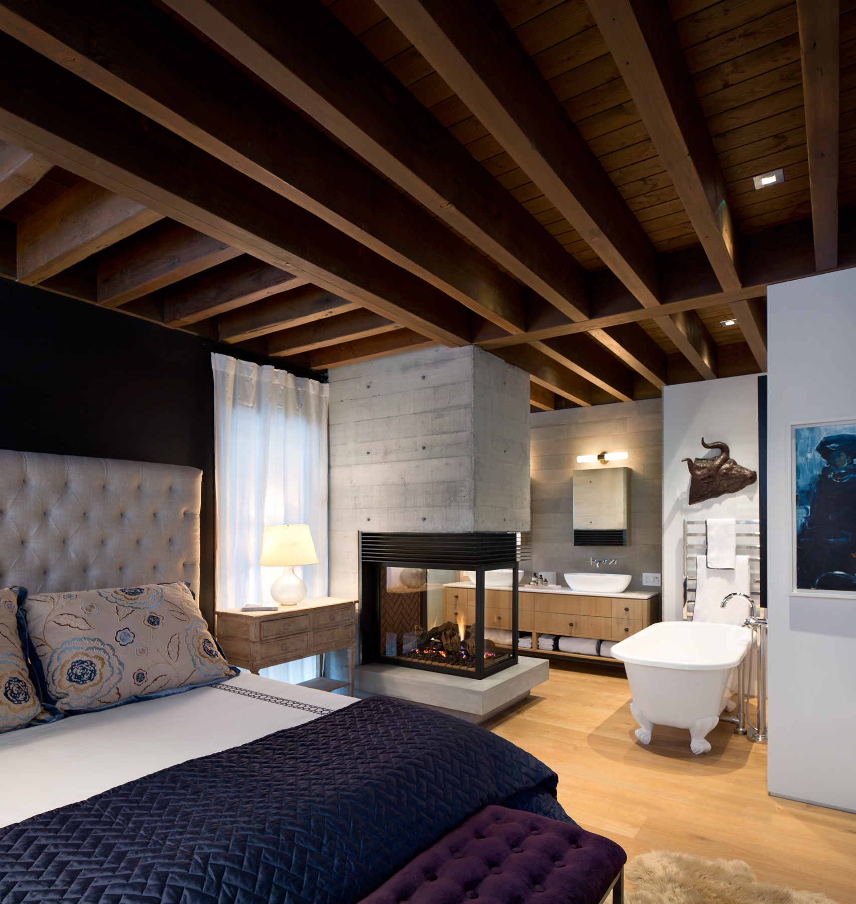 Bedroom with exposed wooden beams, fireplace, freestanding bathtub, and stylish decor—perfect for custom homes in British Columbia.