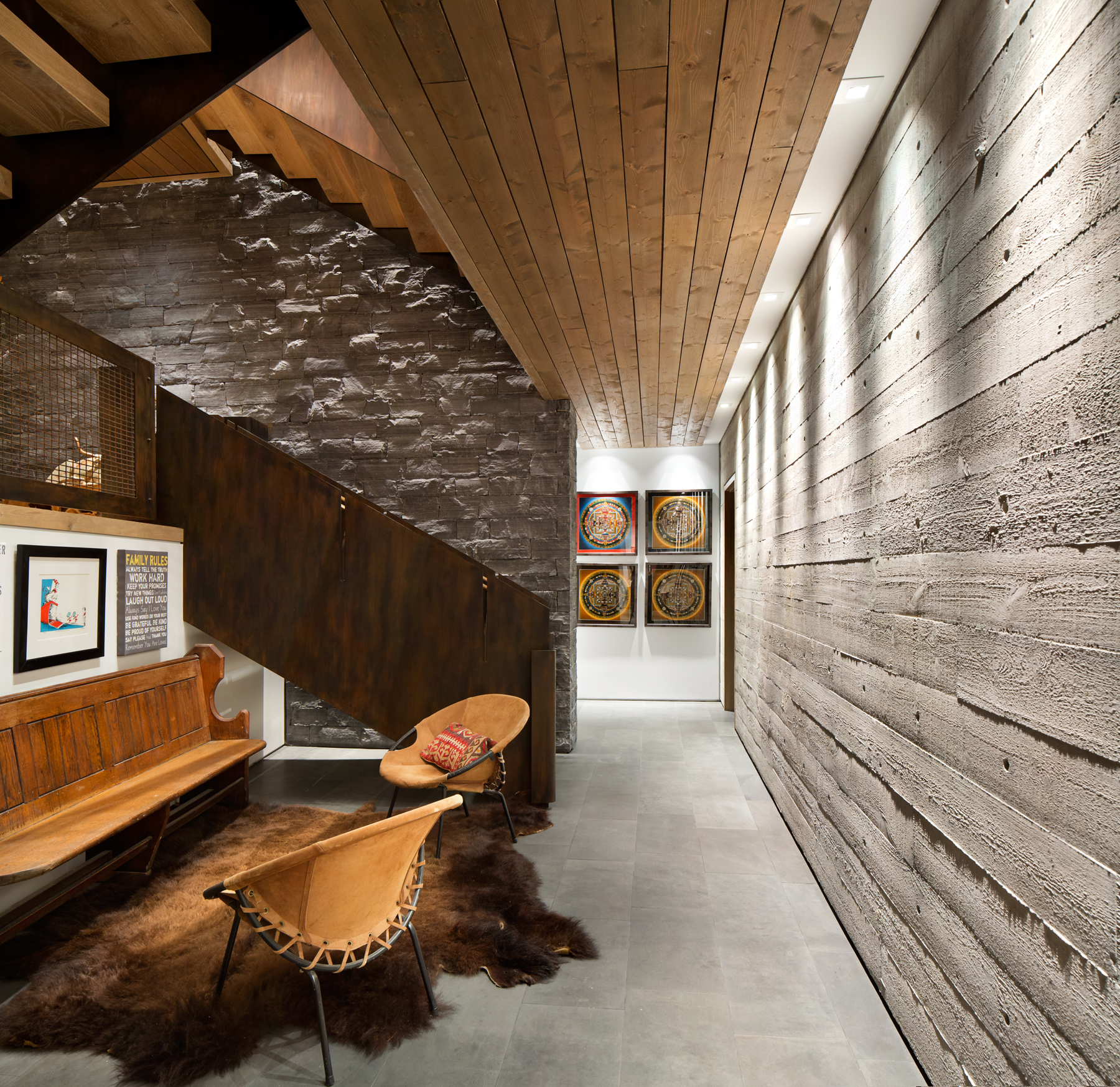 Hallway in a Vancouver custom home with textured walls, wooden ceiling, art displays, and leather chairs on a cowhide rug.