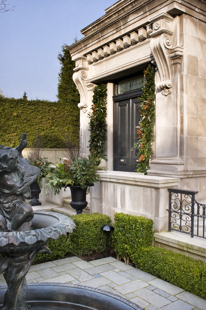 Stone building entrance with a black door, lush greenery garlands, and classical architectural details, showcasing timeless architecture in the heart of British Columbia.