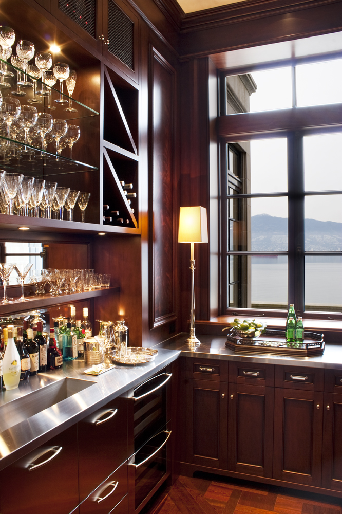 A stylish home bar by a leading British Columbia general contractor, featuring glassware, bottles, and a window overlooking a lake and mountains.