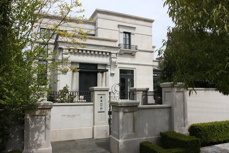 White mansion with black-trimmed windows, a gated entrance, and surrounding greenery showcases stunning architecture inspired by the elegance of Vancouver, British Columbia.
