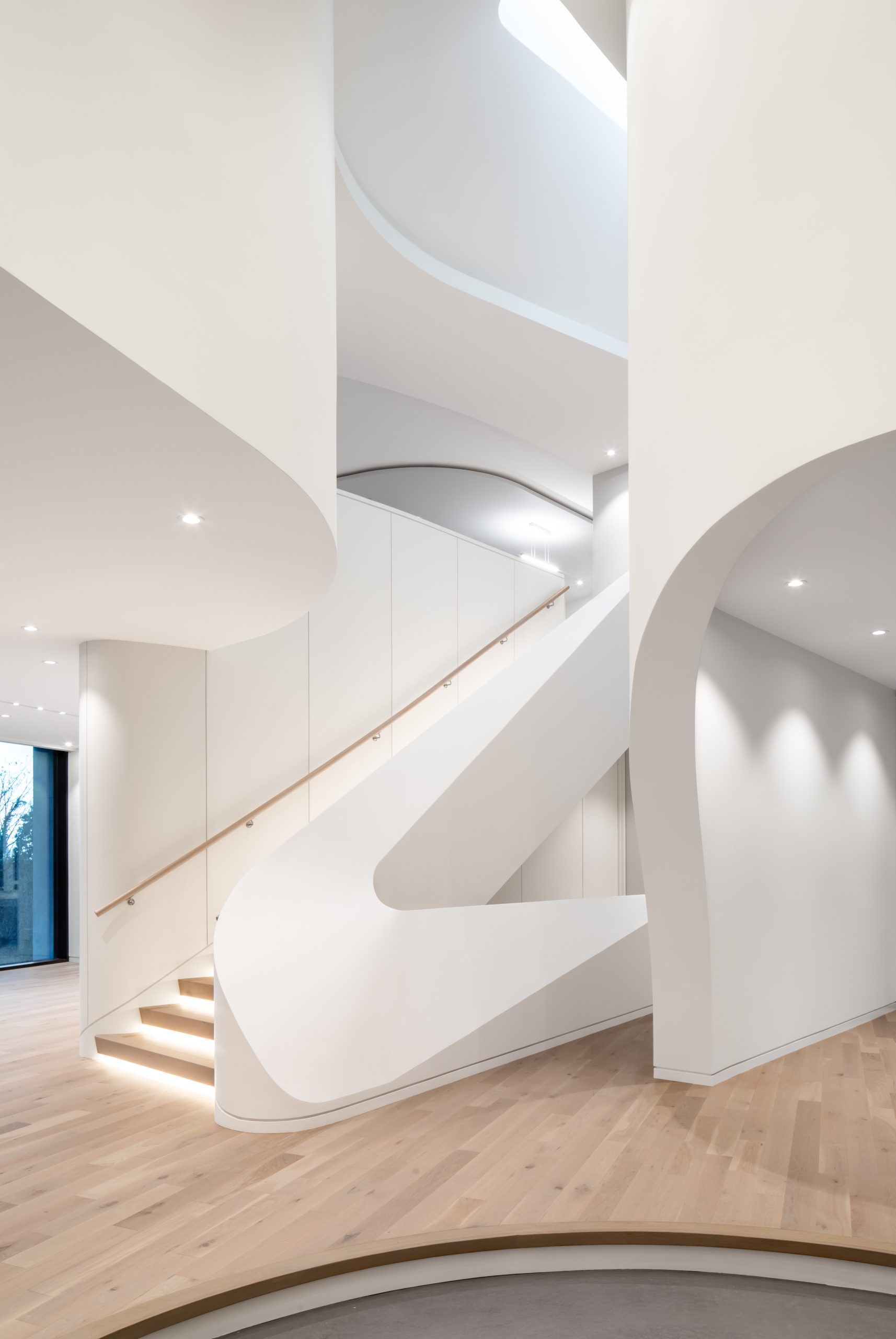 White spiral staircase with curved walls and wooden steps in a bright, minimalist interior space by a leading general contractor.