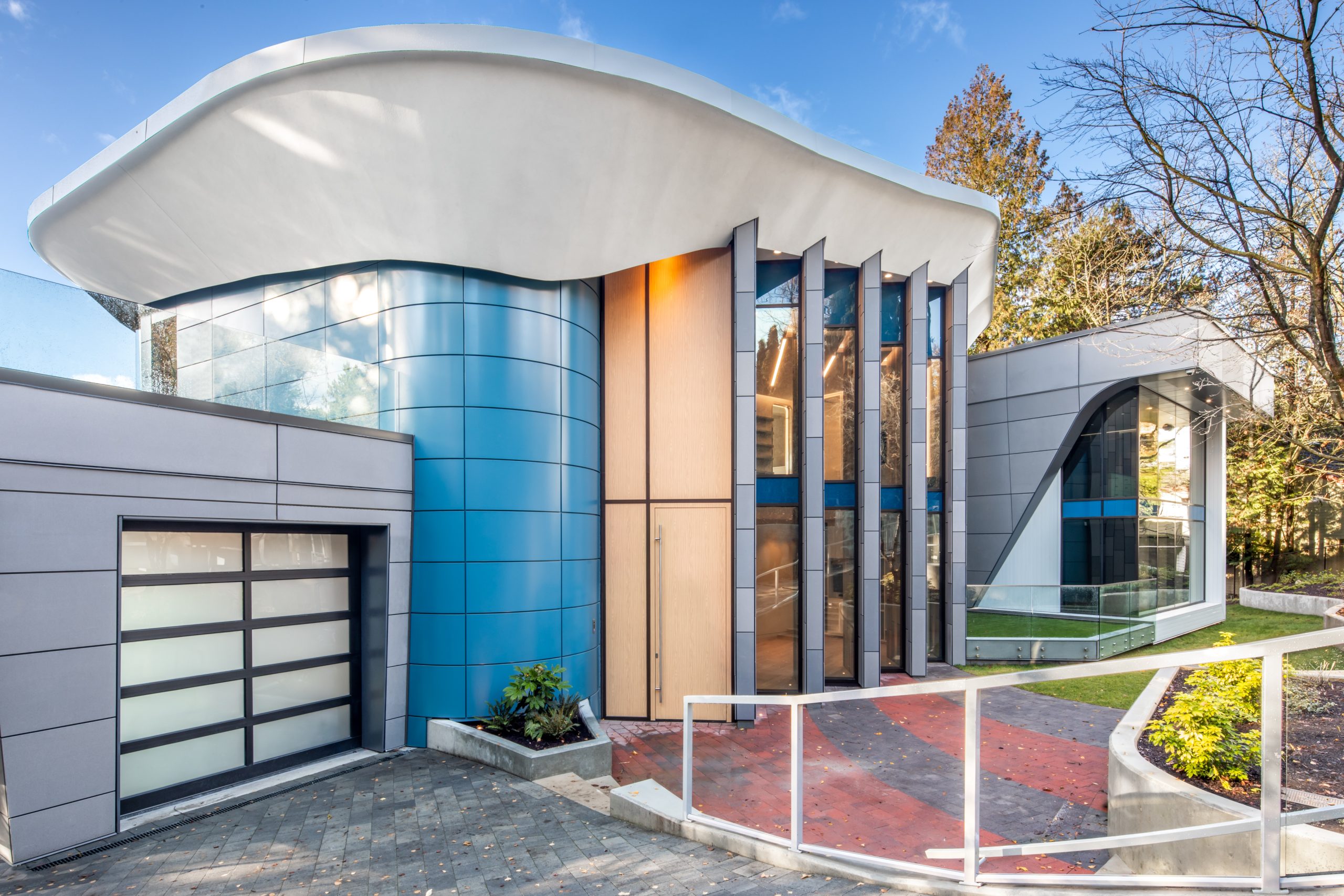 House with blue curved walls, large windows, and a white wavy roof, surrounded by trees—an inspiring example of custom homes and innovative architecture.