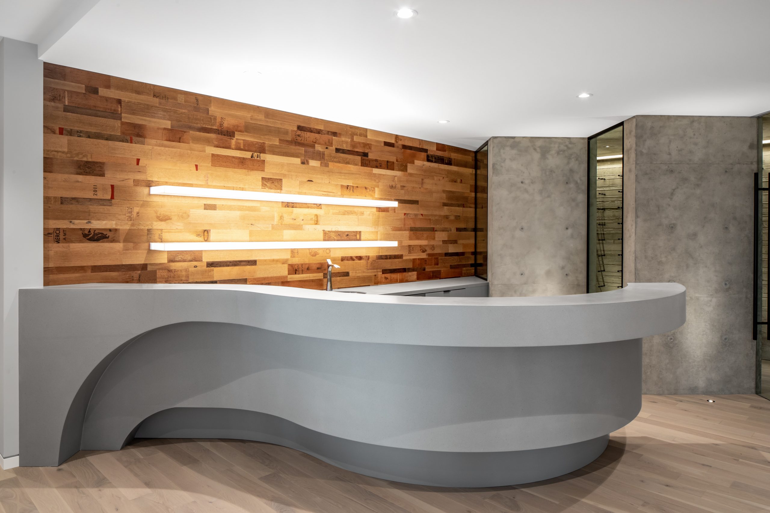 Curved modern reception desk with wood panel wall and minimalist lighting creates a clean, contemporary space perfect for any company in Vancouver, BC.