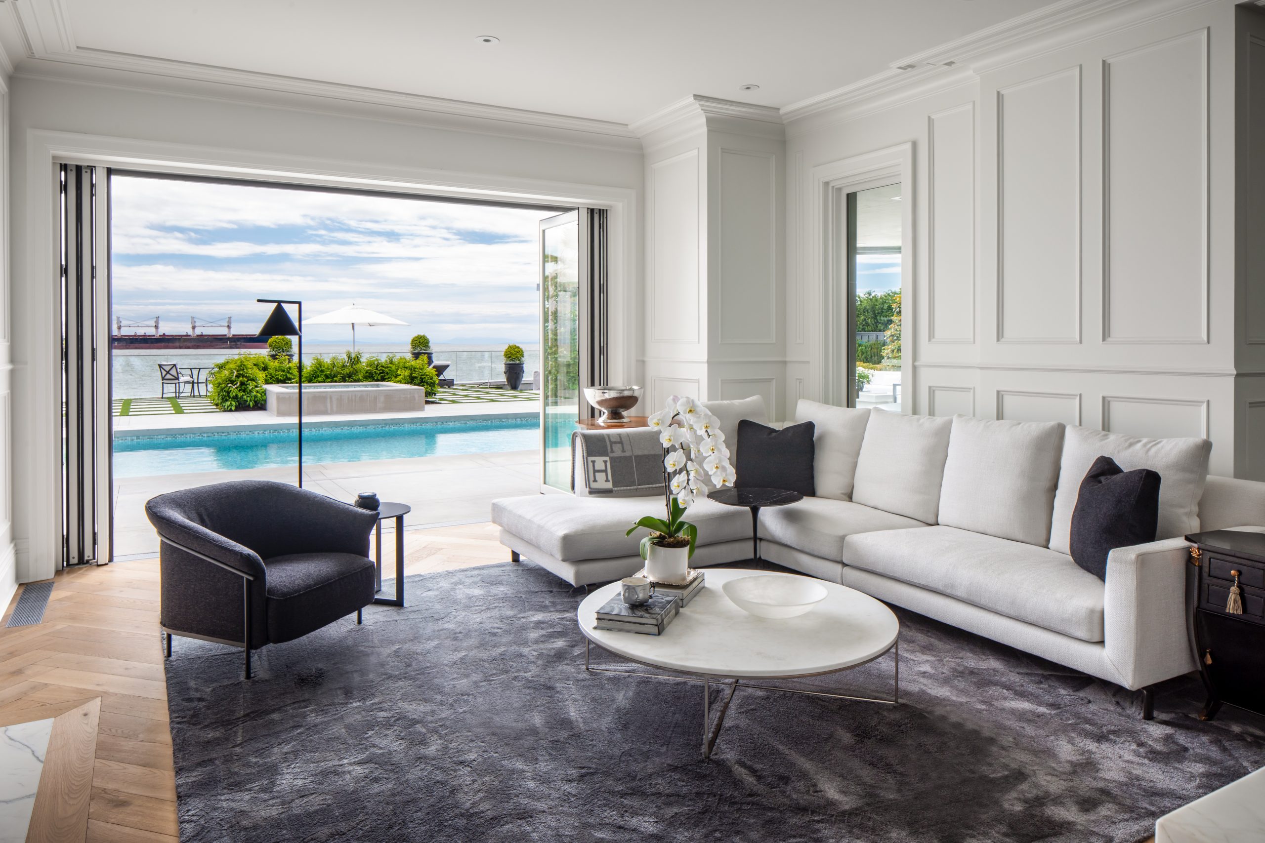 Living room with white sofa, black chair, and open doors revealing a stunning ocean view—an example of Vancouver architecture in custom homes.