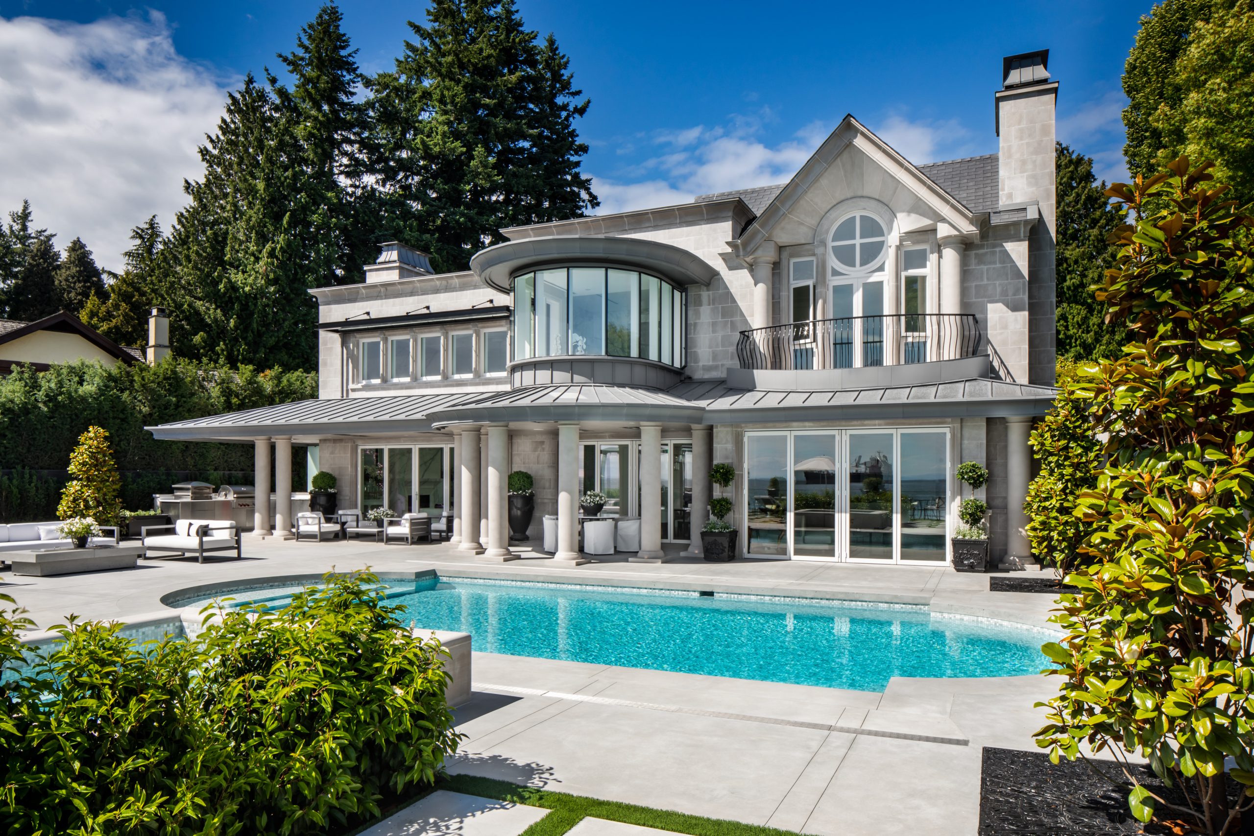 Luxury mansion in Vancouver with large windows, balcony, columns, and a swimming pool in front, surrounded by greenery.