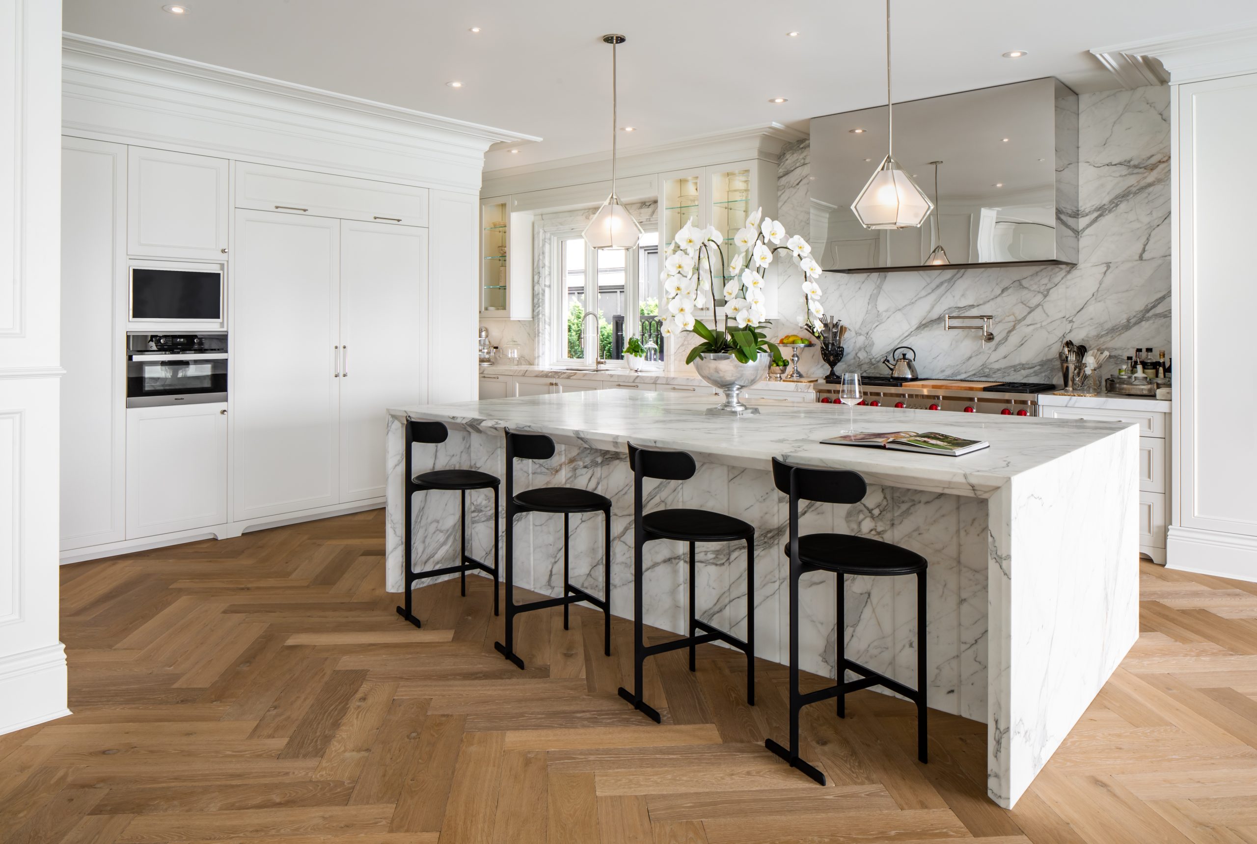 Kitchen with marble island, four black barstools, wood floors, and white cabinetry—expertly crafted by a reputable company specializing in custom homes across British Columbia.