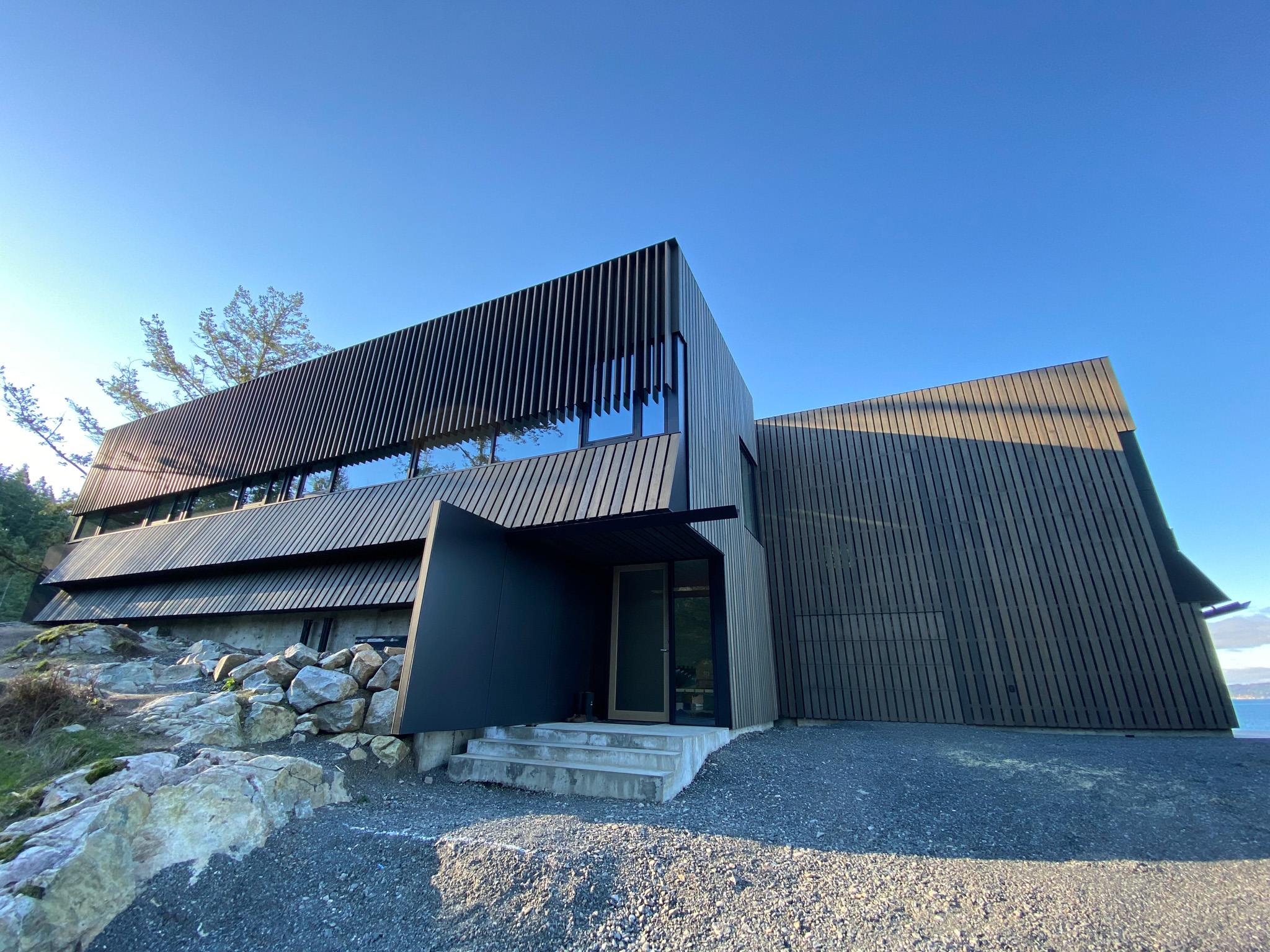Angular building with dark slatted exterior, large windows, and stone steps, set against a clear blue sky in Vancouver, British Columbia.